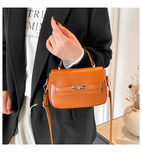 Dettaglio borsa a tracolla marrone con fibbia metallica su completo blazer nero