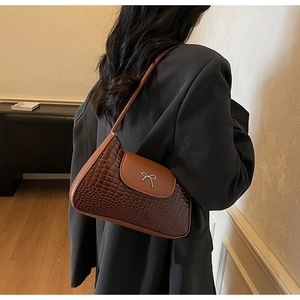 Detail of a brown crocodile-pattern underarm bag with a silver metal bow buckle