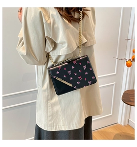Detail view of black PU leather crossbody bag with pink bow pattern and golden chain