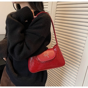 Close-up of red crocodile pattern texture and silver bow detail on the underarm bag