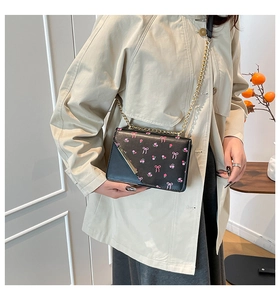 Lifestyle shot of a black small square bag with pink bows and floral patterns on beige coat