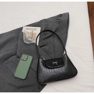 Close-up of black croc-effect underarm bag with silver bow detail on white fabric background