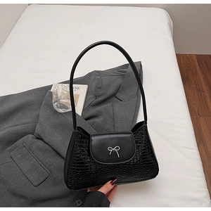 Detail of black faux crocodile leather bag with silver bow ornament on a grey blazer