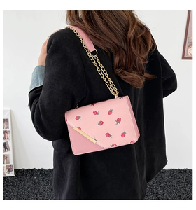 Rear view of a model wearing a pink crossbody bag with sweet strawberry print and gold chain