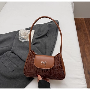 Detail of dark brown crocodile texture bag with silver bow accent and leather flap