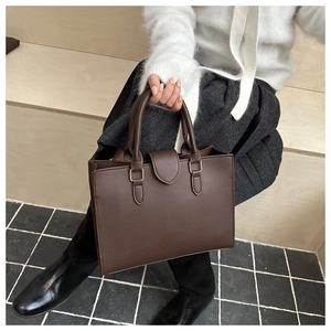Dettaglio della borsa tote in pelle marrone scuro tenuta da una modella sulle scale