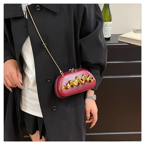 Detail of burgundy clutch with golden wave metal trim and fine chain strap on model