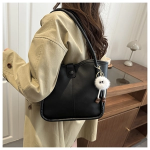 Detail view of a black faux leather bucket bag with a plush monster charm on a model's shoulder