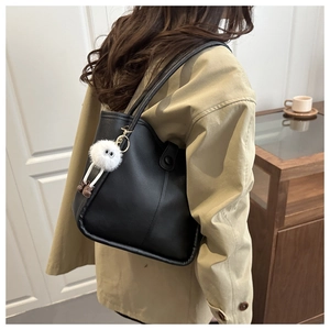 Close-up of black PU leather tote bag featuring a cute white plush doll keychain charm