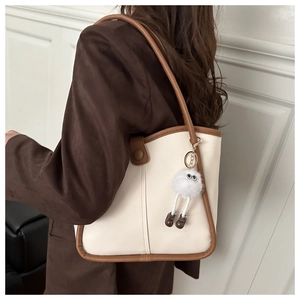 Detail of minimalist cream bucket bag with brown trim and plush charm worn by a model