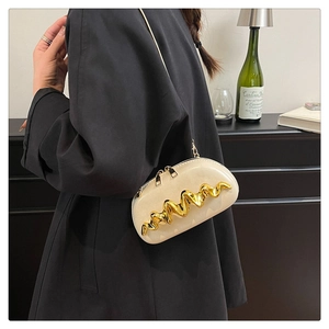 Detail of cream leather crossbody bag with bold gold wavy metal trim and chain strap