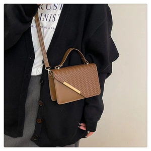 Detail einer braunen Handtasche mit Fischgrätmuster und elegantem goldenem Metallbesatz