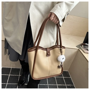 Detail of a two-tone beige and brown faux leather tote bag with a plush charm on handle