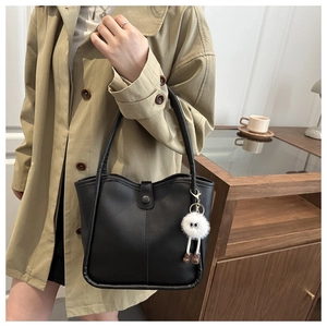 Detail of a chic black leather underarm bag with a cute white plush monster keychain charm