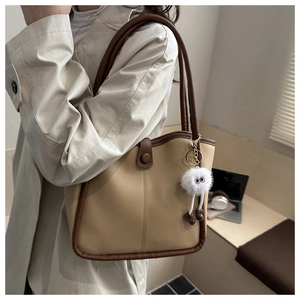 Detail view of large faux leather tote bag with stylish plush pendant and contrast stitching