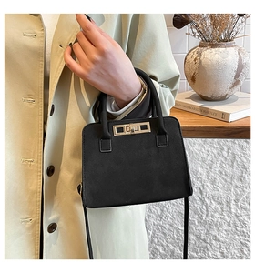 Detail of a black matte leather trapezoid handbag with elegant gold clasp and handle