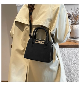 Detail of a matte black handbag with a golden twist lock on a beige trench coat