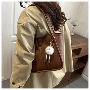 Detail of dark brown leather tote bag with a cute white plush monster charm on the strap
