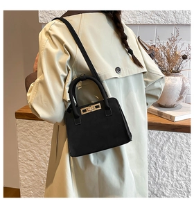 Detailed back view of a black suede handbag with gold lock on a female model