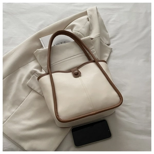 Close-up of contrast trim detail and button closure on cream leather shoulder bag
