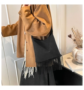 Detail view of a black suede handbag featuring dense long fringe and a slim shoulder strap