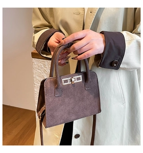 Detailed close-up of dark brown suede handbag with metal lock and dual handles