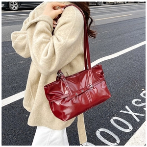 Detail of red patent leather shoulder bag with decorative belt straps and silver eyelets