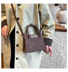 Detail of dark brown suede handbag with golden swivel lock worn with a beige trench coat