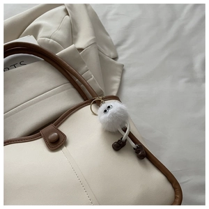 Charming white plush doll bag charm with big eyes and tiny brown shoes on a canvas bag