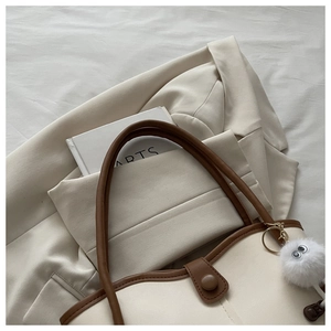 Detail of beige tote bag with brown leather trim and cute plush monster charm