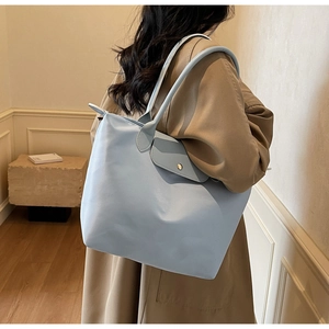 Detail view of light blue nylon tote bag with leather flap and snap button closure