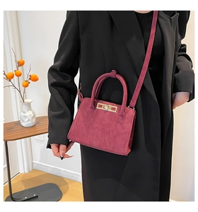 Close-up of a burgundy suede crossbody bag with gold turn-lock worn by a model in a suit
