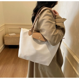 Side view of white nylon tote bag with brown leather handles and gold clasp detail