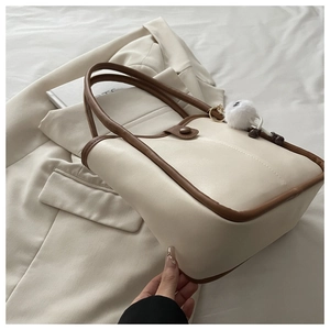 Close-up of cream faux leather shoulder bag with brown trim and plush ball charm