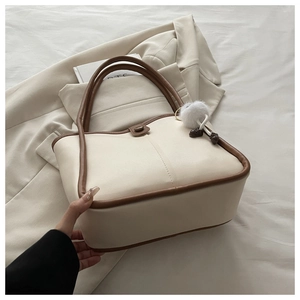Detail view of the cream and brown contrast shoulder bag with a soft white pompom charm
