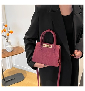 Detail of burgundy suede handbag with gold lock shown on model wearing black blazer