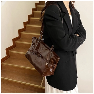 Brown glossy tote bag with buckle detail shown being worn by a model on a shoulder