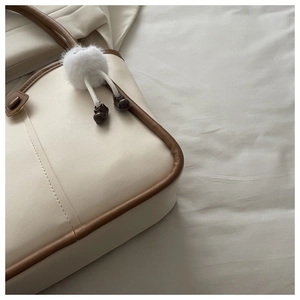Detailed close-up of cream leather tote bag with contrast piping and plush pendant