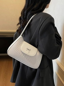 White faux crocodile leather underarm bag with silver bow accent on model side profile