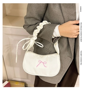 Detail of cream shoulder bag with pink bow embroidery and ruffled handle on grey blazer
