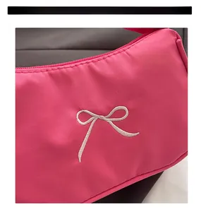 Detail of hot pink nylon shoulder bag featuring white embroidered bow and zip closure