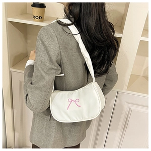Close-up of minimalist cream white crescent shoulder bag with pink bow embroidery detail