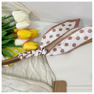 Close-up of minimalist beige tote bag handle decorated with brown polka dot silk scarf