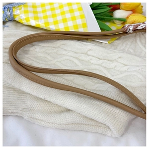 Detail of brown leather bag strap with dual stitching on white knit sweater texture