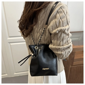 Detalle de bolso saco de cuero negro con cordón, cadena dorada y letras de metal