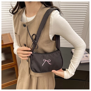 Detail of black nylon crescent shoulder bag with pink bow embroidery on white model outfit