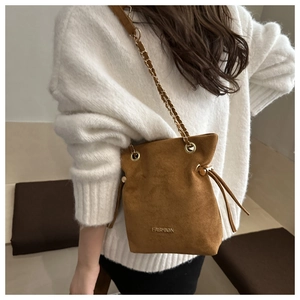 Detalle de bolso saco de ante marrón con texto FASHION y correa de cadena metálica