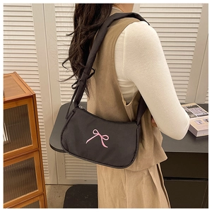 Close-up of black nylon shoulder bag with pink embroidered bow and wide strap details