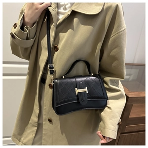Close-up of black quilted handbag with gold H-buckle worn by a model in a trench coat