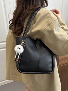 Minimalist black leather tote bag with unique plush monster charm on a stylish model